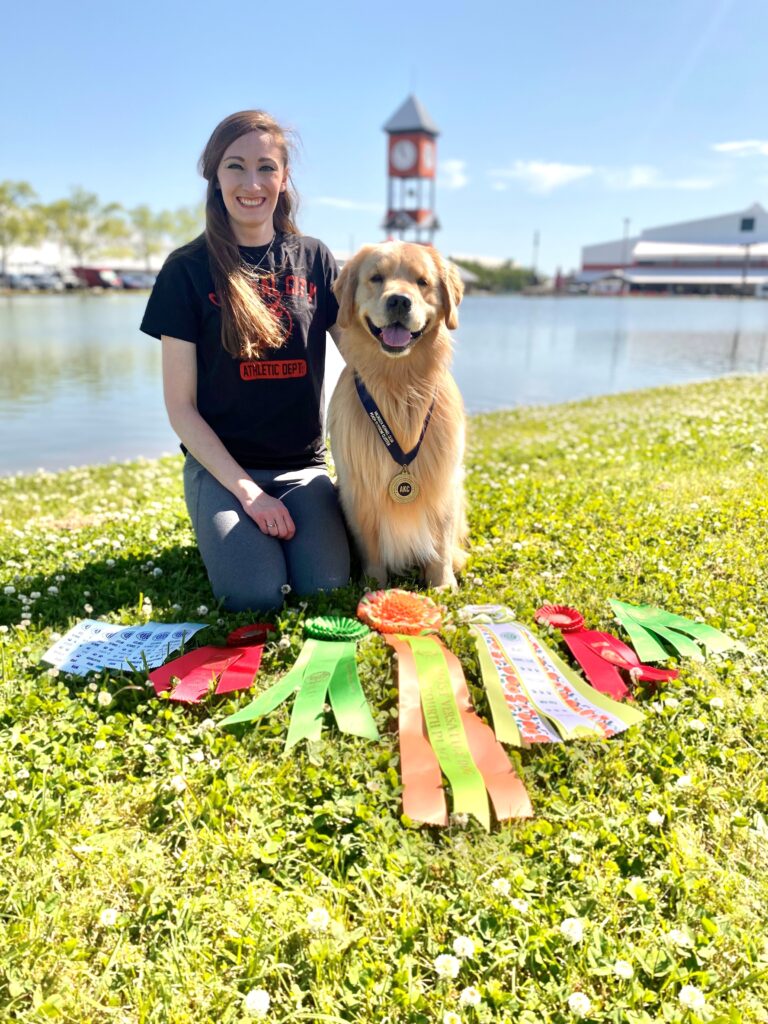 Taylor with a golden retriever and multiple ribbons and medal